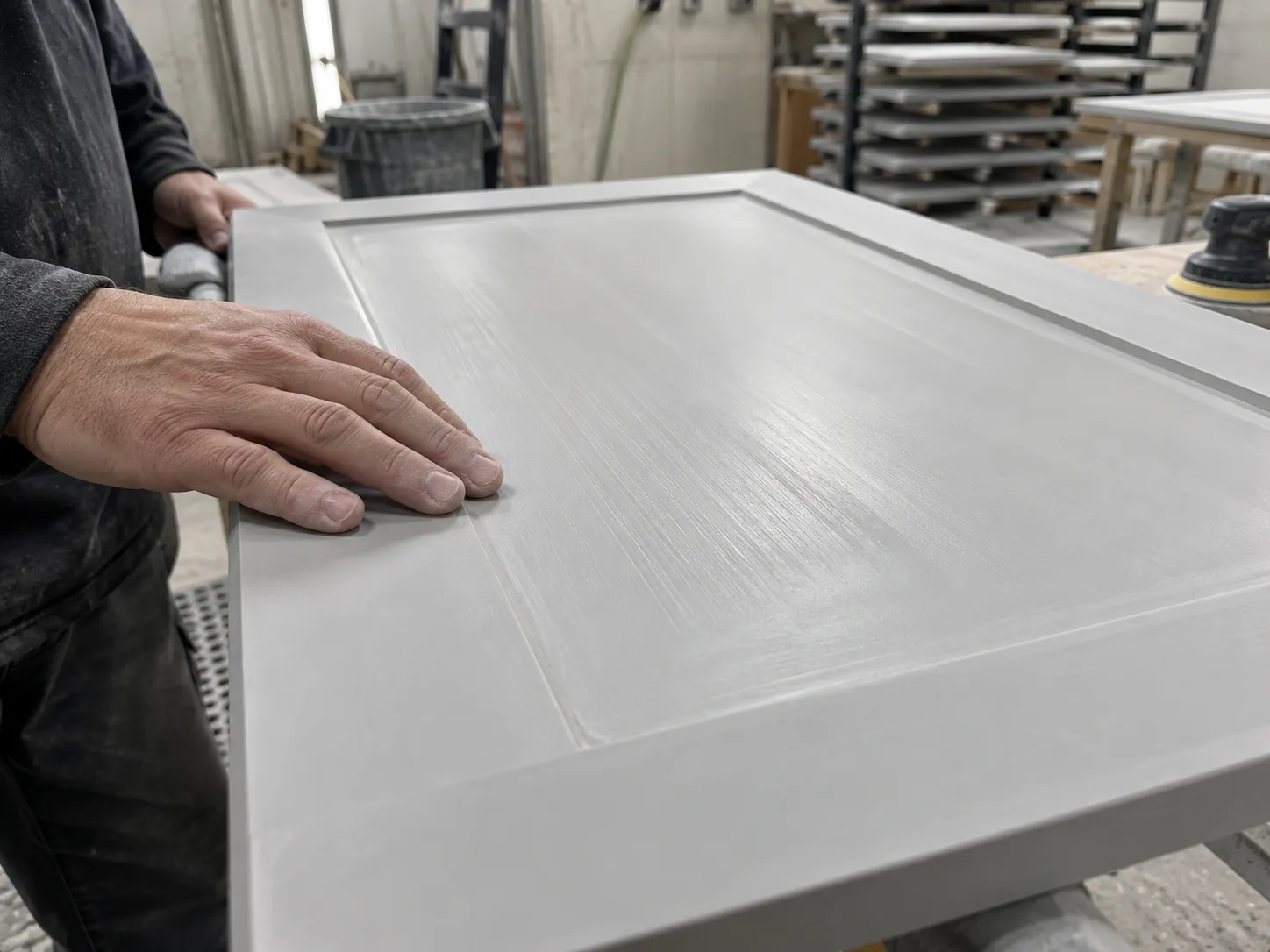 Operator checking a primer-coated cabinet door surface by hand in the finishing area