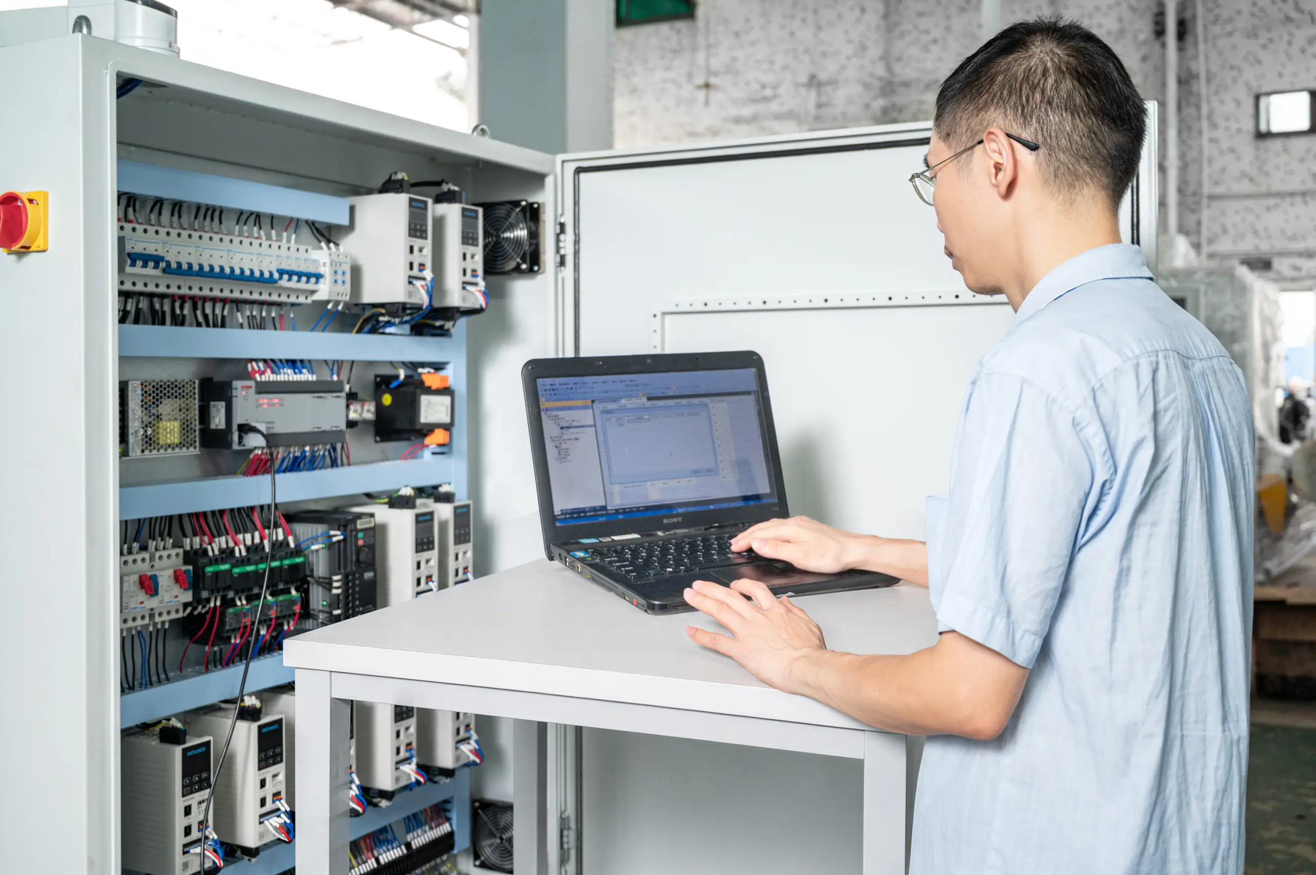 Engineer programming a sanding-machine control cabinet with a laptop during outgoing electrical testing