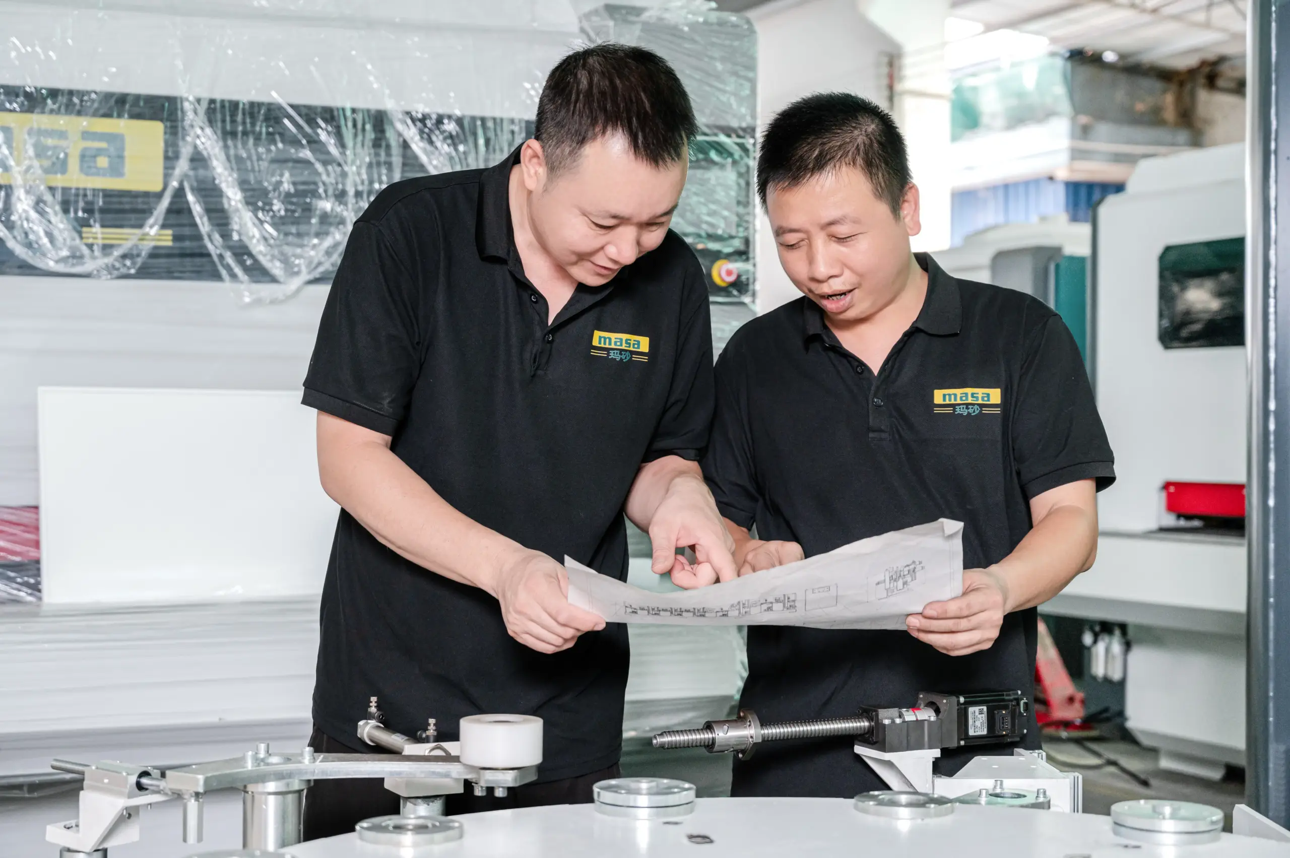 MASA engineers reviewing a machine drawing beside the sanding table before configuration