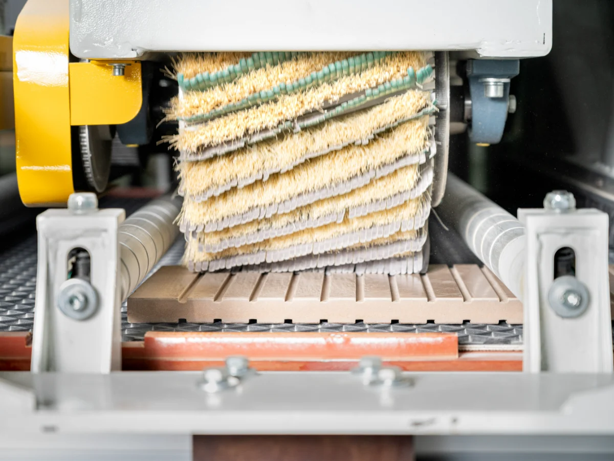 Coated cabinet panel passing through a floating-head sanding machine, with the smooth primer surface and sanding units visible
