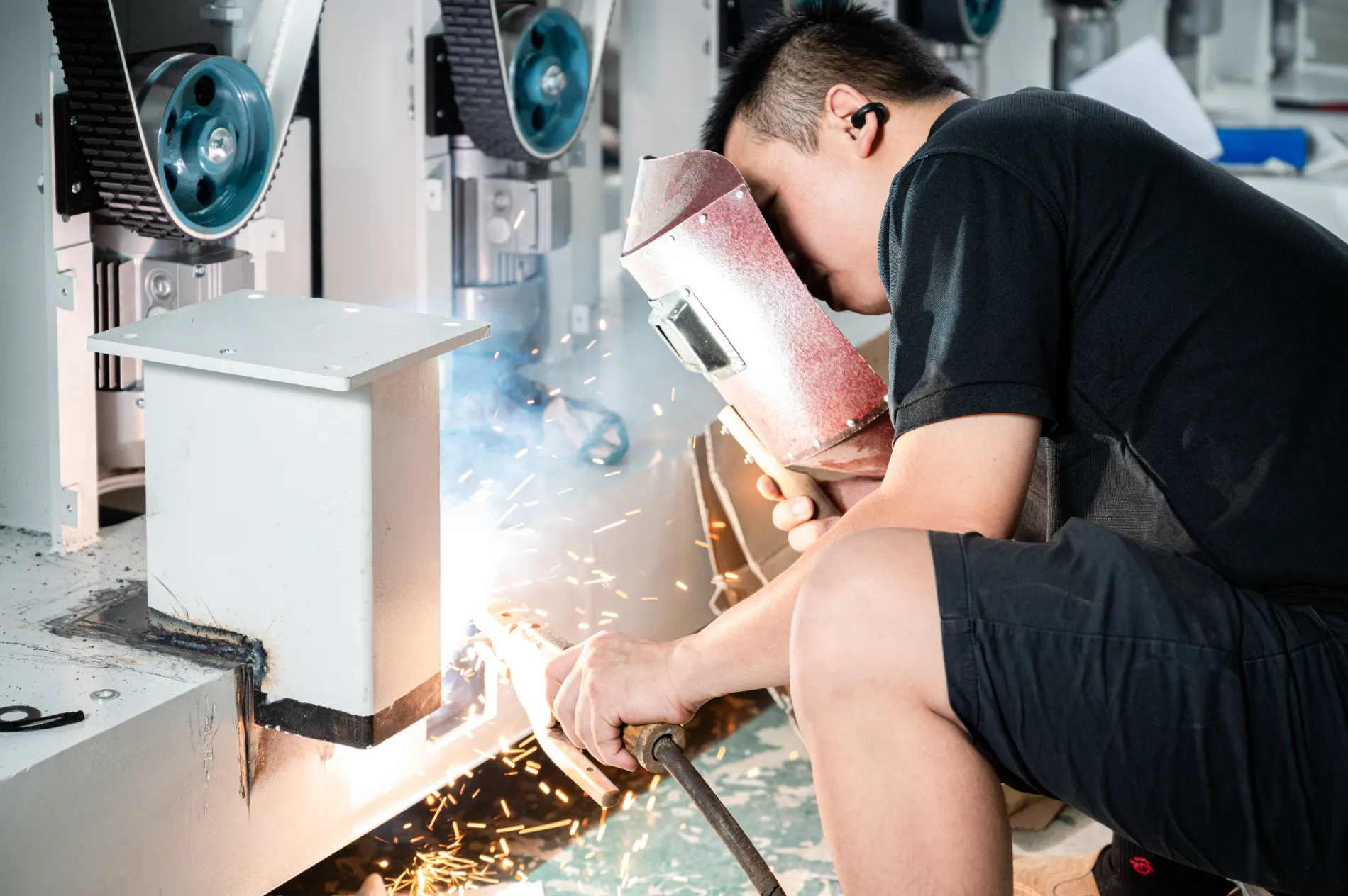 Technician welding a sanding-machine frame in the Foshan sheet-metal workshop