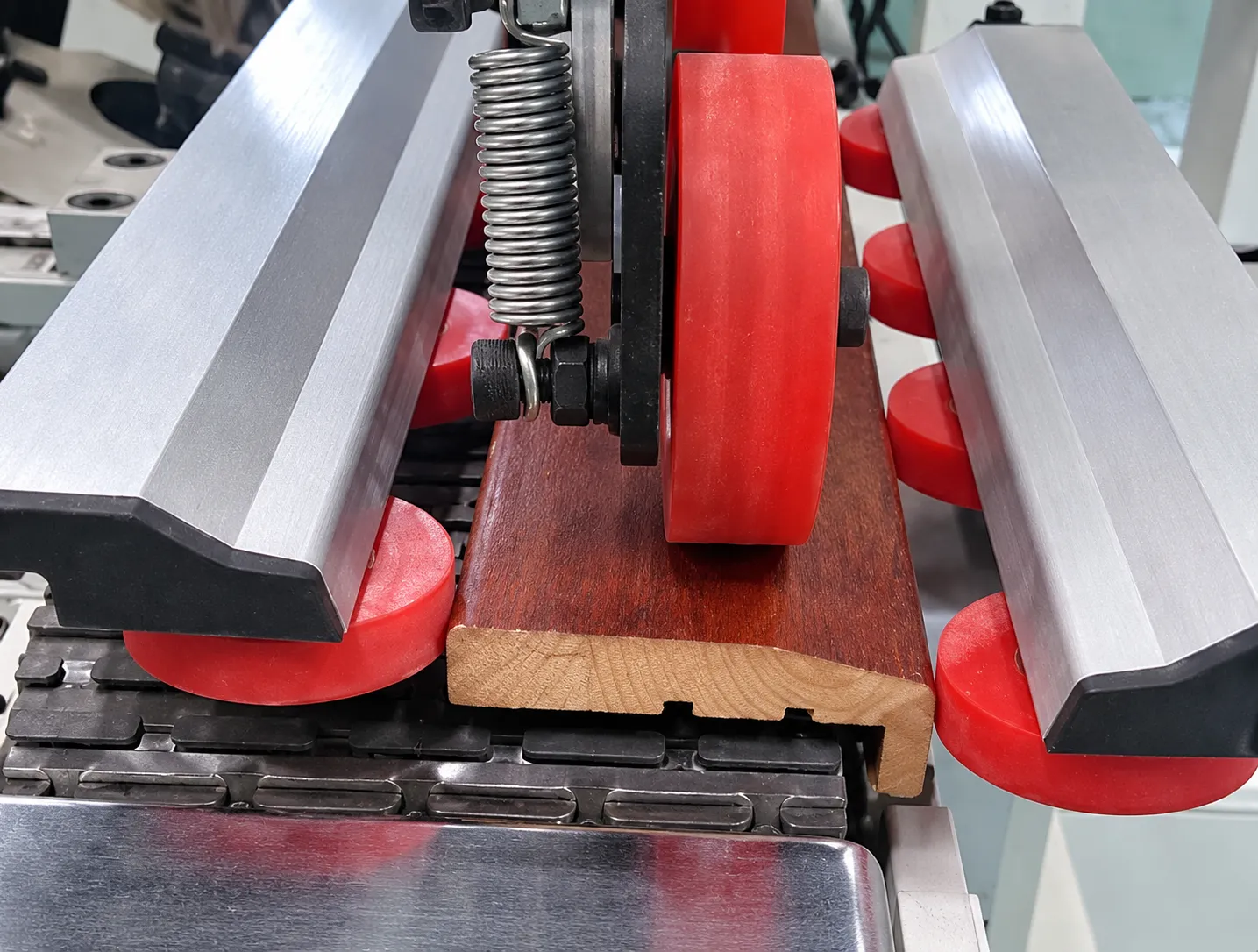 Moulding sanding machine processing a wood profile between hold-down rollers