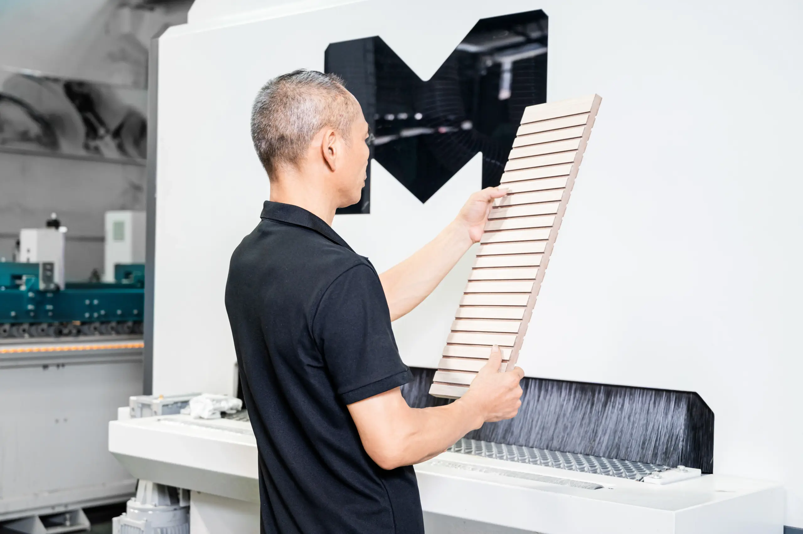 Operator inspecting a slatted wooden workpiece beside a sanding machine
